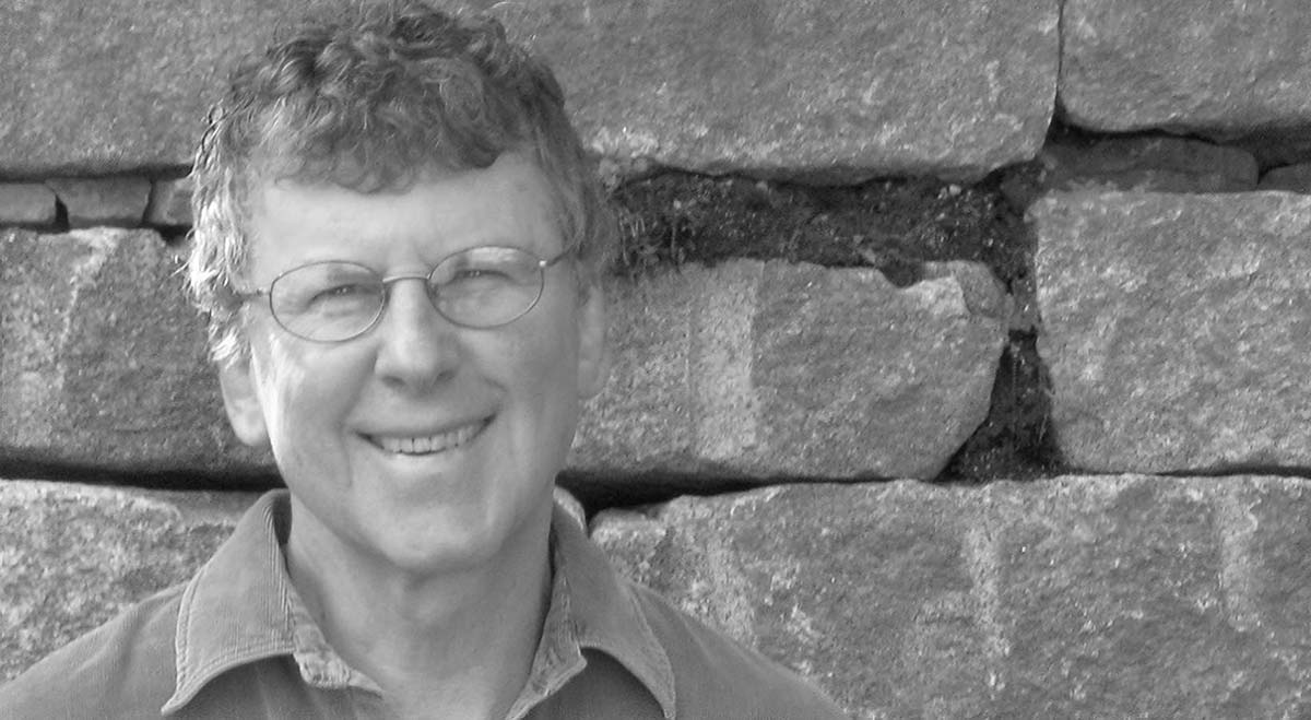 Black-and-white head-and-shoulders portrait of the author smiling in front of a stone wall.